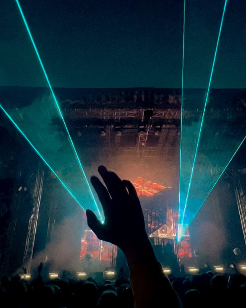 A raised hand reaching toward laser beams above a festival stage